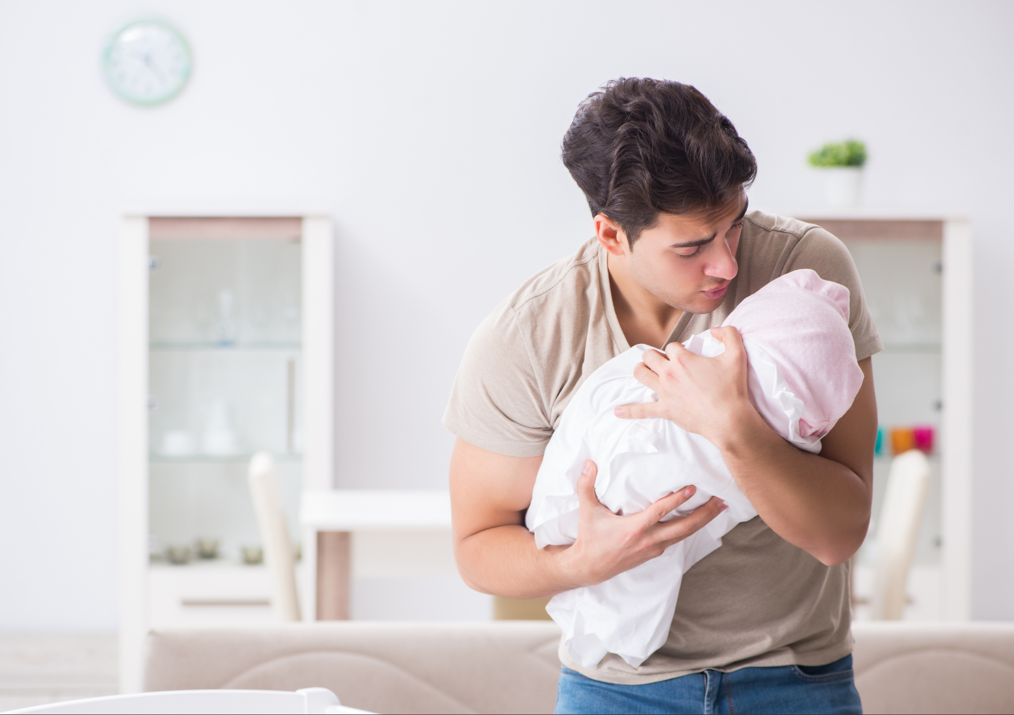 Pai segurando recém nascido enrolado em manta, em casa, em momento de carinho e cuidado com o bebê.